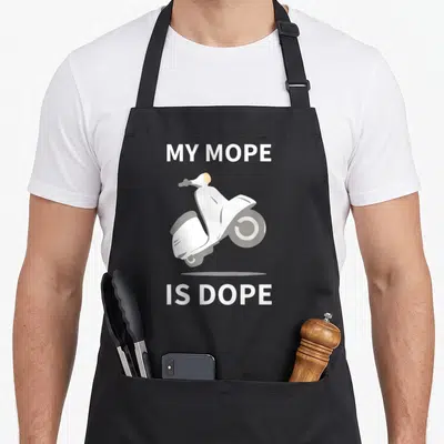 Mope scooter apron - White moped illustration with MY MOPE IS DOPE text stacked vertically — shown on a black cotton canvas apron against a white background