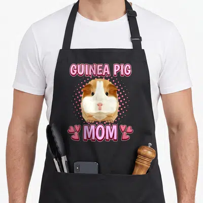 Guinea pig mother's day aprons - Cartoon brown and white guinea pig over pink dots with GUINEA PIG MOM text and four — shown on a black cotton canvas apron against a white background