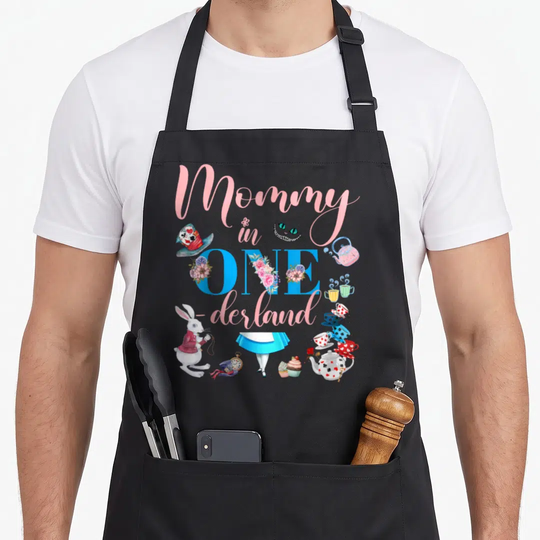 Alice family aprons - Mommy in ONEderland text with rabbit, cat, tea set, and skirt in pink blue and red watercolor — shown on a black cotton canvas apron against a white background