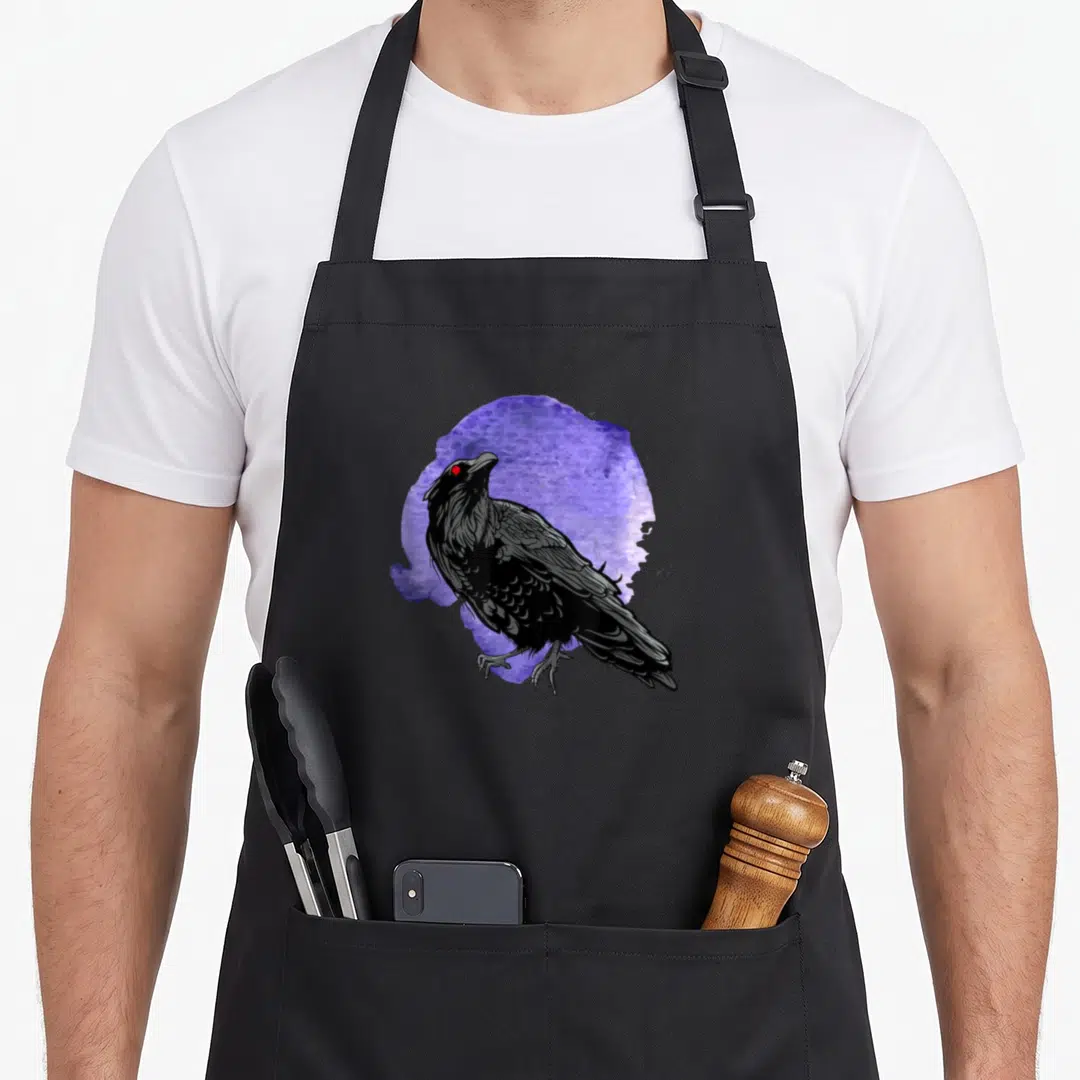 Crow raven bird apron - Black crow with red eyes positioned in front of a purple watercolor splash design — shown on a black cotton canvas apron against a white background