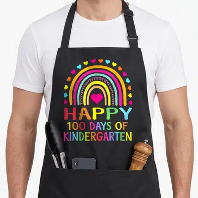 Kindergarten rainbow apron - Colorful rainbow with hearts and Happy 100 Days of Kindergarten text — shown on a black cotton canvas apron against a white background