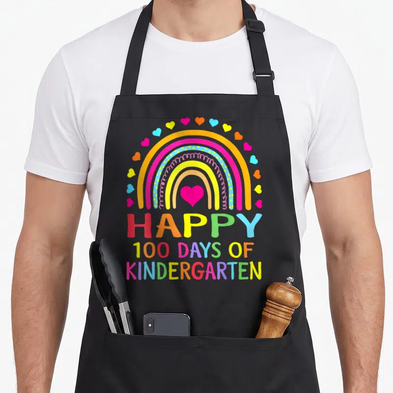 Kindergarten rainbow apron - Colorful rainbow with hearts and Happy 100 Days of Kindergarten text — shown on a black cotton canvas apron against a white background