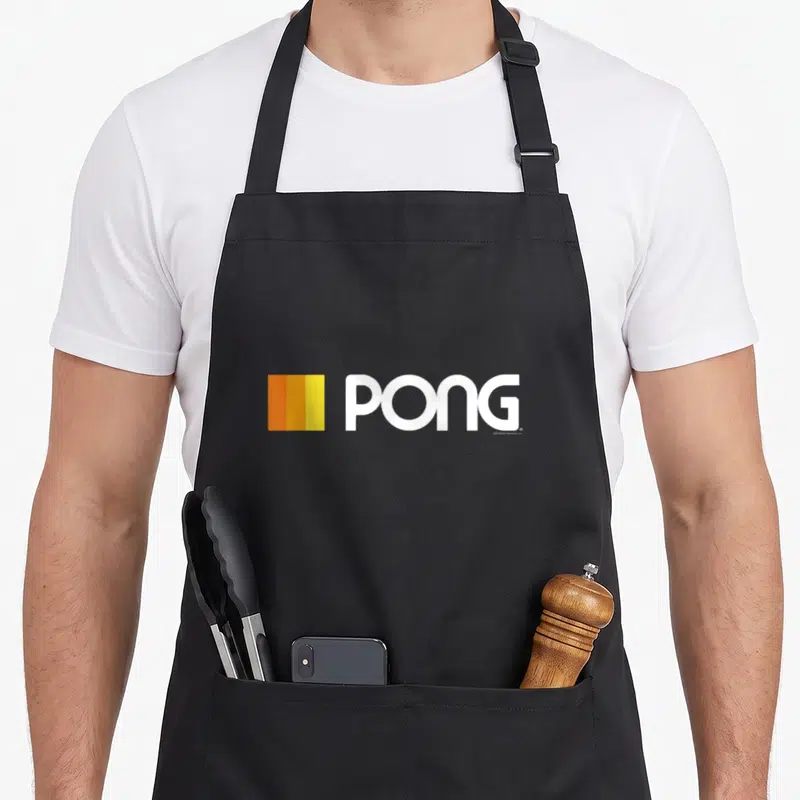 Pong gamer retro apron - White PONG text beside three vertical orange and yellow bars — shown on a black cotton canvas apron against a white background