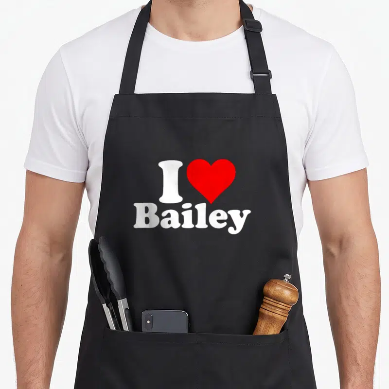 Funny baileys apron - White text I and Bailey with a red heart symbol on black fabric — shown on a black cotton canvas apron against a white background