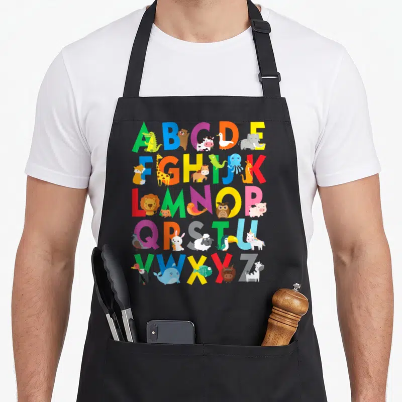 Learning animal apron - Colorful A-Z alphabet grid with cartoon animals standing next to letters — shown on a black cotton canvas apron against a white background
