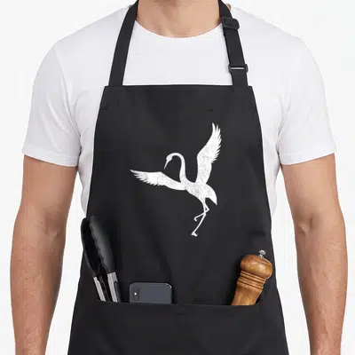 Sandhill sparrow dad apron - White distressed crane silhouette with spread wings and trailing legs on grey background — shown on a black cotton canvas apron against a white background