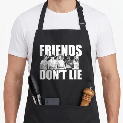 Lie shot friends cooking apron - White text FRIENDS DON'T LIE above five teenagers in grey and black photo style — shown on a black cotton canvas apron against a white background