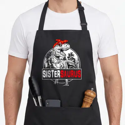 Family t-rex apron - Sistersaurus text banner over T-Rex with red bandana and sunglasses inside white circle — shown on a black cotton canvas apron against a white background