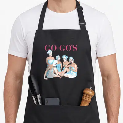 Beat beauty apron - GO-GO'S text above five women in blue towels and white face masks — shown on a black cotton canvas apron against a white background