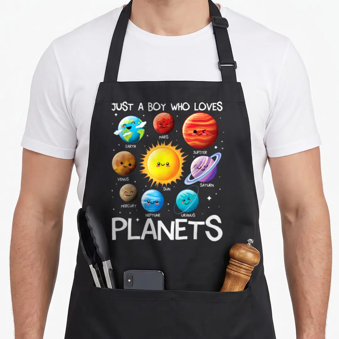 Planet solar science apron - Cartoon solar system with labeled planets and central sun under Just A Boy Who Loves — shown on a black cotton canvas apron against a white background