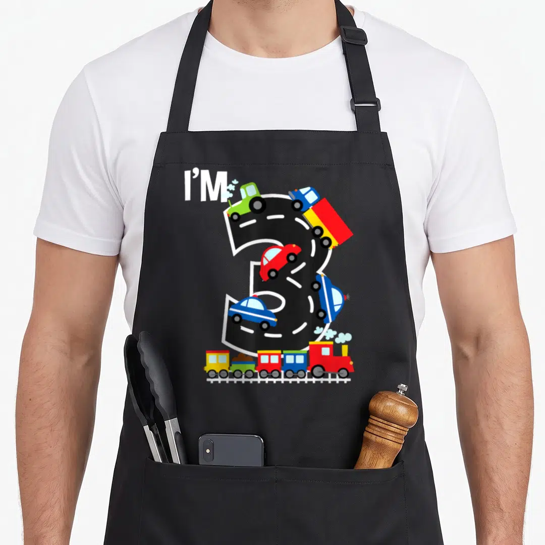 Train truck apron - I'M 3 road design with cars and train in red blue green yellow cartoon style — shown on a black cotton canvas apron against a white background