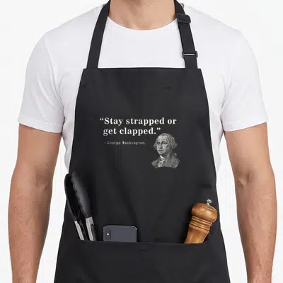 Stay 2nd apron - George Washington portrait beside Stay strapped or get clapped quote in white minimalist style — shown on a black cotton canvas apron against a white background