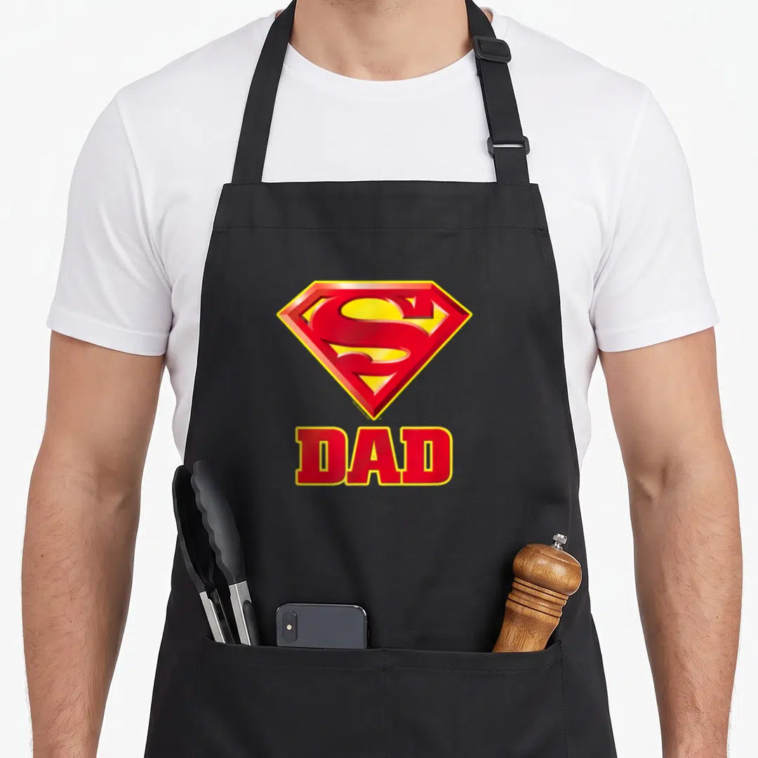 Funny robin dad apron - Red and yellow shield logo above bold red DAD text on black fabric — shown on a black cotton canvas apron against a white background