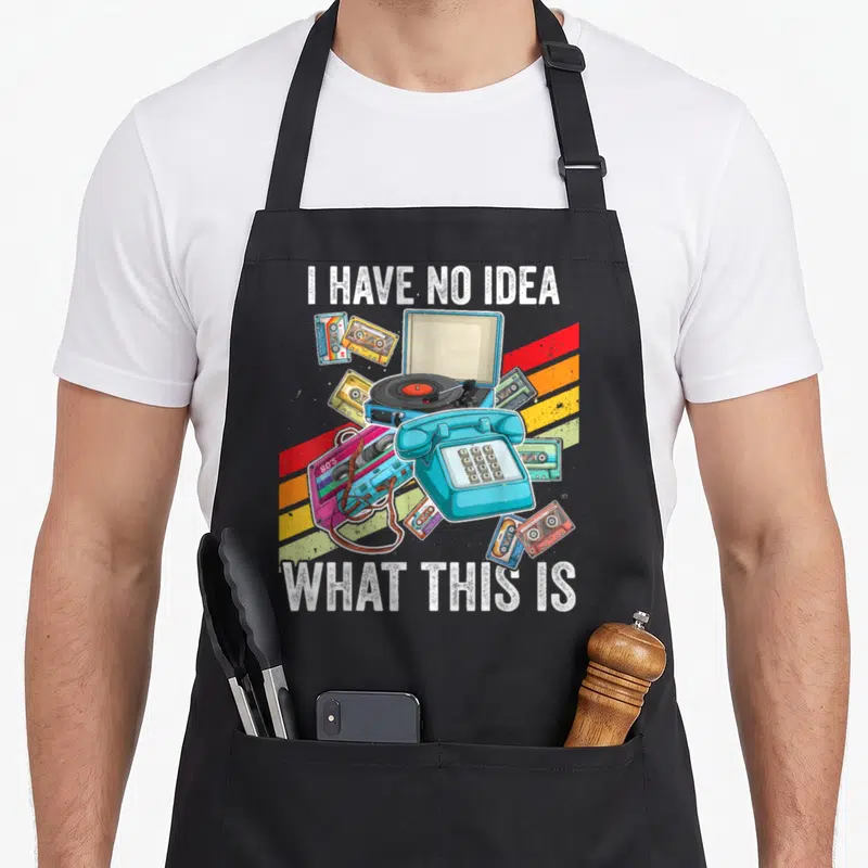 Funny 70s chef outfit with apron - I HAVE NO IDEA WHAT THIS IS text surrounding retro phone turntable and tapes — shown on a black cotton canvas apron against a white background