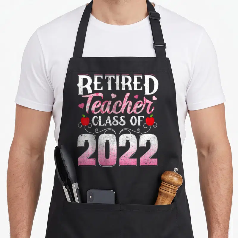 Teacher funny retirement aprons - Stacked text reading Retired Teacher Class of 2022 with red apples and pink hearts — shown on a black cotton canvas apron against a white background