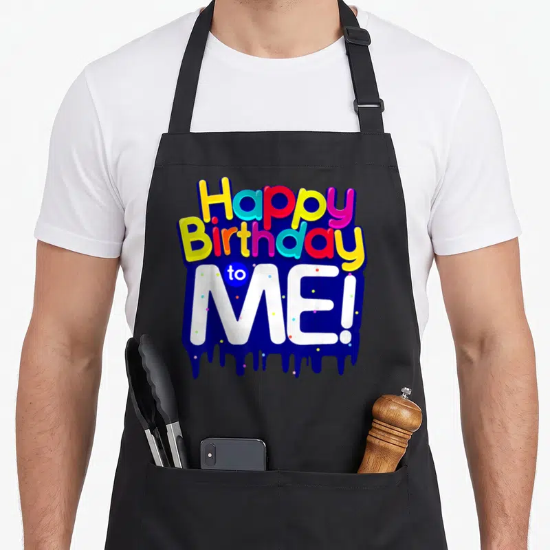 Age born day apron - Stacked colorful text Happy Birthday to ME! over blue dripping shape with scattered dots — shown on a black cotton canvas apron against a white background