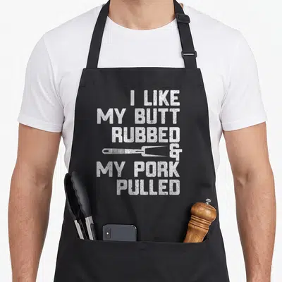 Rubbed pulled addict apron - White stacked text I like my butt rubbed and my pork pulled with meat fork — shown on a black cotton canvas apron against a white background