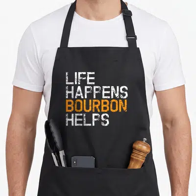 Happen bourbon apron - Stacked LIFE HAPPENS BOURBON HELPS text in white and orange distressed typography — shown on a black cotton canvas apron against a white background