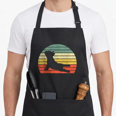 Yoga french apron - Grey dog silhouette in stretch pose against green yellow orange and red striped circle — shown on a black cotton canvas apron against a white background