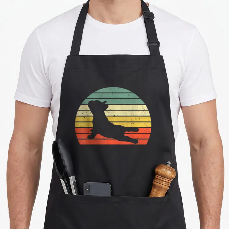 Yoga french apron - Grey dog silhouette in stretch pose against green yellow orange and red striped circle — shown on a black cotton canvas apron against a white background