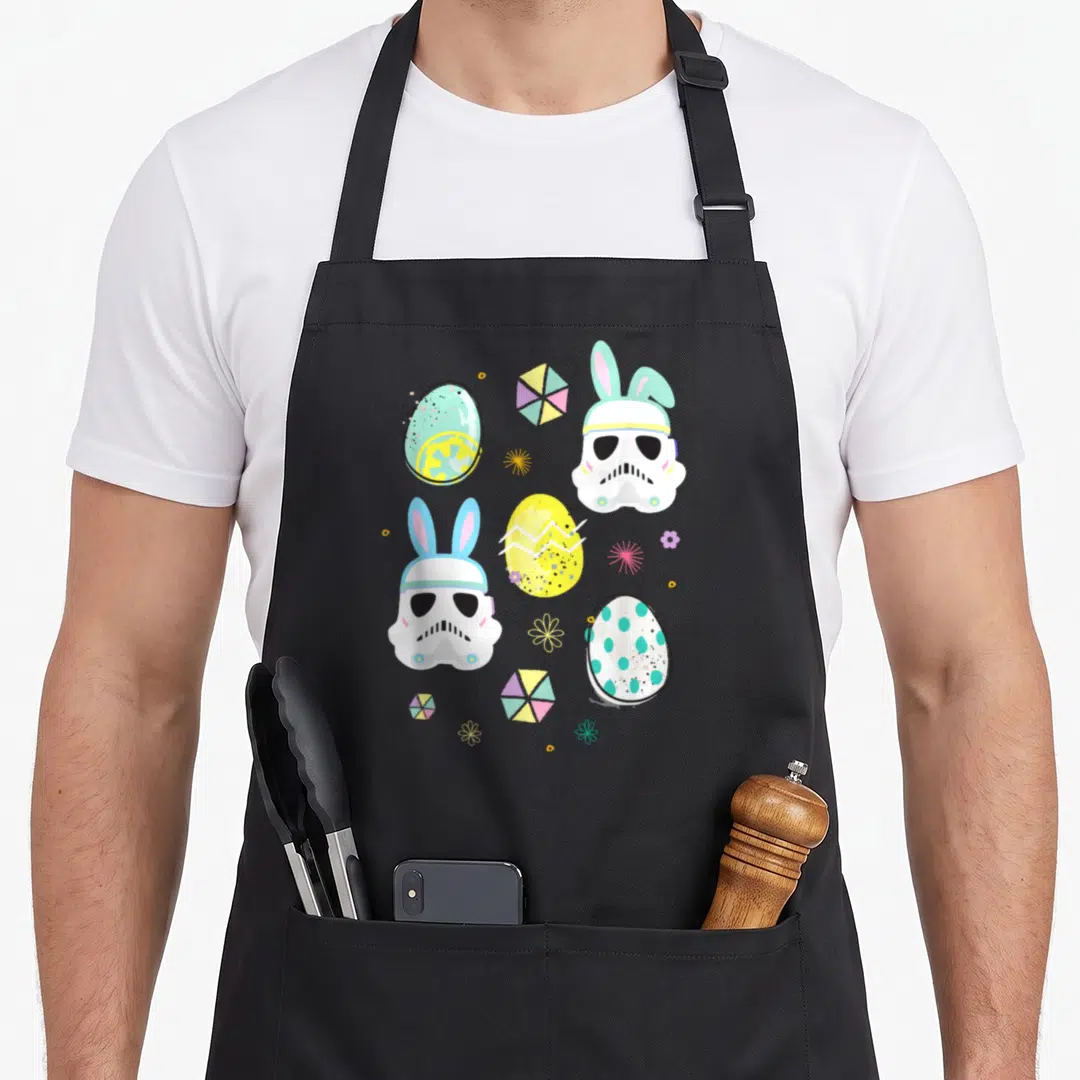 Bunny easter egg apron - Cartoon Stormtrooper helmets with pastel bunny ears and decorated Easter eggs in white blue — shown on a black cotton canvas apron against a white background