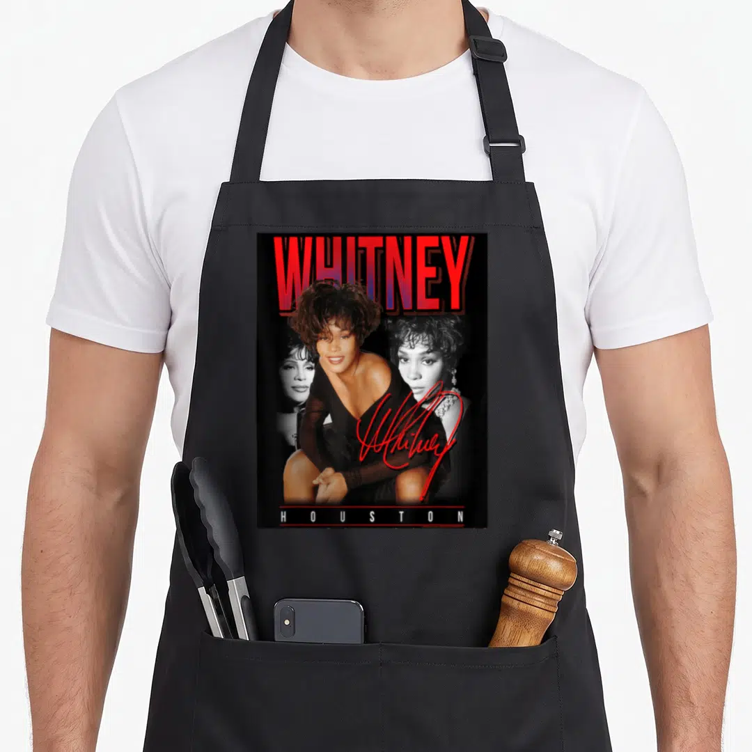 Whitney photo collage apron - Red WHITNEY text, three overlapping portraits, red signature, white HOUSTON text on black — shown on a black cotton canvas apron against a white background