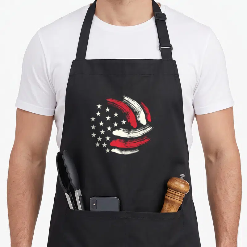 Patriotic volleyball american flag apron - Red and white brushstrokes form a ball next to white stars on grey background — shown on a black cotton canvas apron against a white background