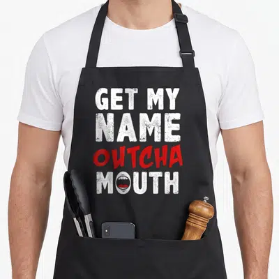 Outcha gossip apron - Distressed white and red text GET MY NAME OUTCHA MOUTH with mouth graphic in O — shown on a black cotton canvas apron against a white background