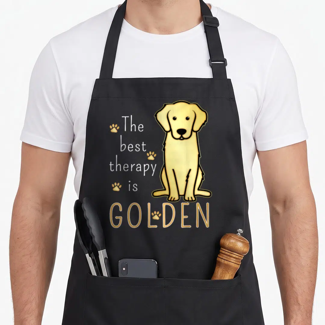 Therapy golden retriever apron - Cartoon golden dog sitting next to stacked text The best therapy is GOLDEN — shown on a black cotton canvas apron against a white background
