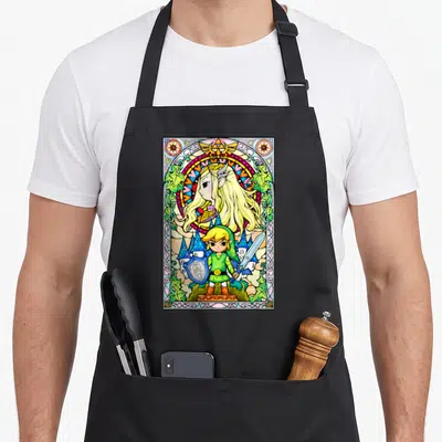 Link stained apron - Chibi Link and Zelda in stained glass style with castle and Triforce symbol — shown on a black cotton canvas apron against a white background