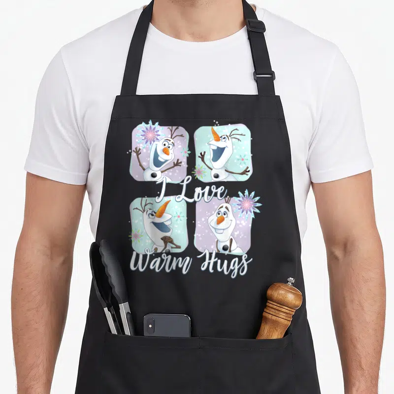 Frozen colorful apron - Four Olaf portraits in white blue purple grid with I Love Warm Hugs script — shown on a black cotton canvas apron against a white background