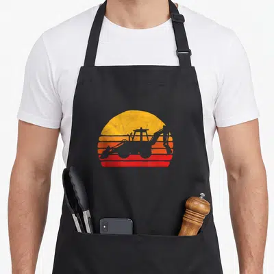 Loader construction apron - Retro backhoe loader silhouette against yellow orange and red striped sunset — shown on a black cotton canvas apron against a white background