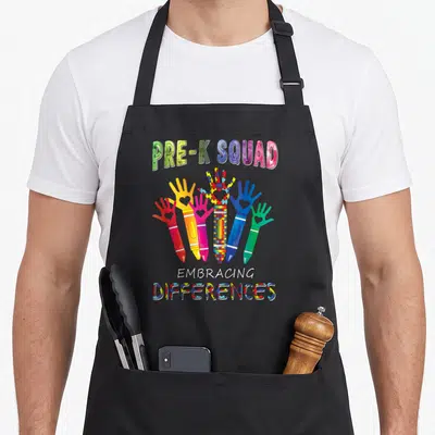 Pre teacher art apron - Five crayon hands in red yellow pink blue green with hearts and puzzle pieces under PRE-K SQUAD — shown on a black cotton canvas apron against a white background