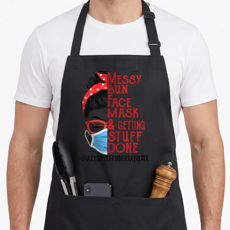 Face messy aprons - Woman in profile with blue mask, red polka dot bandana, glasses, and stacked red text reading Messy — shown on a black cotton canvas apron against a white background