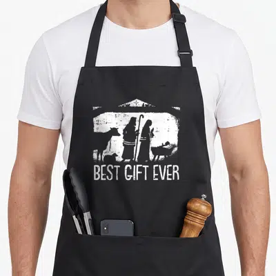 Jesus womens christmas apron - White nativity silhouette above BEST GIFT EVER text on black background — shown on a black cotton canvas apron against a white background