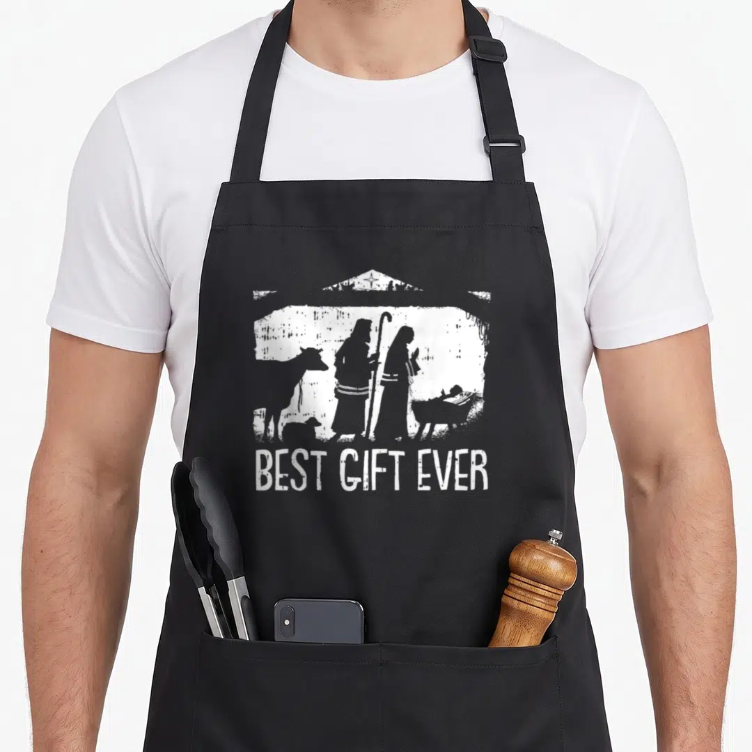 Jesus womens christmas apron - White nativity silhouette above BEST GIFT EVER text on black background — shown on a black cotton canvas apron against a white background