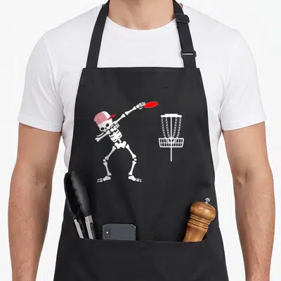 Hat halloween apron - White skeleton in red cap throwing red disc at white disc golf basket — shown on a black cotton canvas apron against a white background