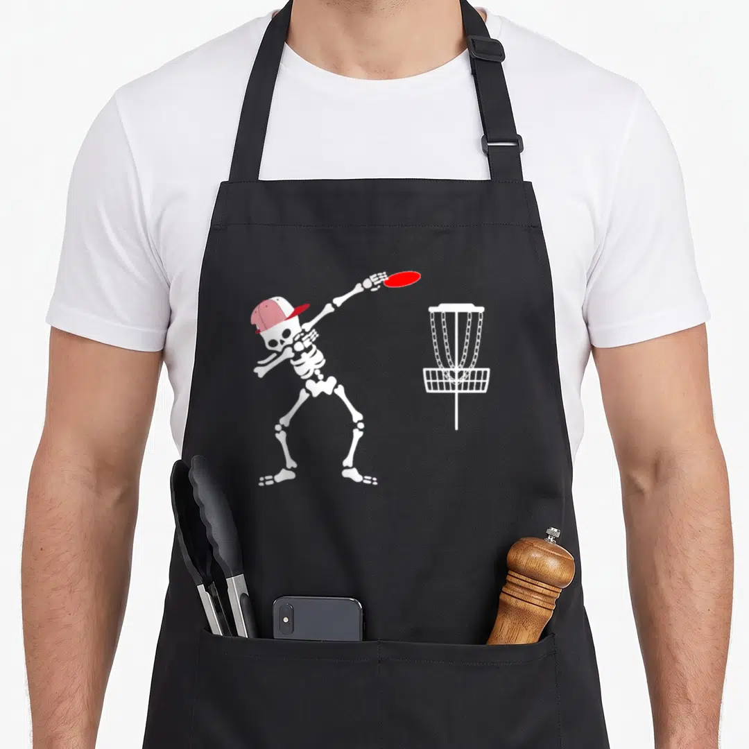 Hat halloween apron - White skeleton in red cap throwing red disc at white disc golf basket — shown on a black cotton canvas apron against a white background