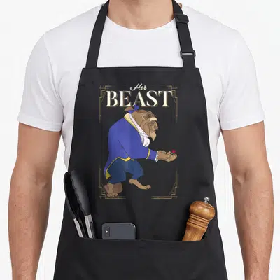 Framed beast mode apron - Stacked text Her BEAST above a cartoon beast in blue holding a rose inside a gold frame — shown on a black cotton canvas apron against a white background