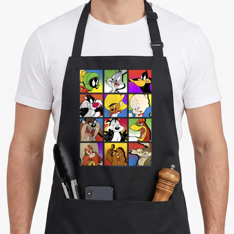 Funny shot box apron - Twelve Looney Tunes portraits in yellow red blue purple grid squares — shown on a black cotton canvas apron against a white background