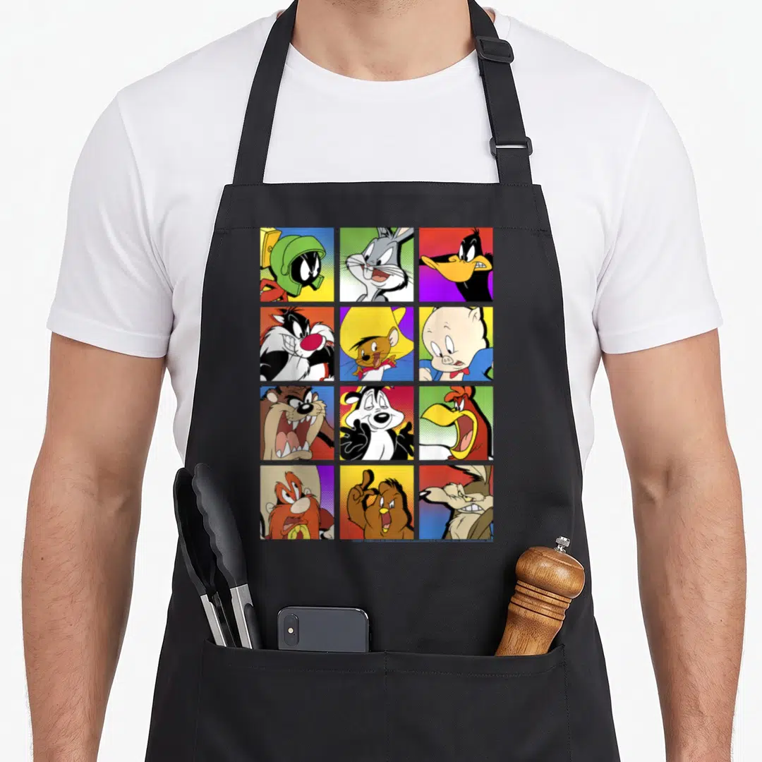 Funny shot box apron - Twelve Looney Tunes portraits in yellow red blue purple grid squares — shown on a black cotton canvas apron against a white background