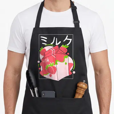 Shake kawaii aprons - Pink strawberry milk carton with Katakana text and strawberries in a white rectangular frame — shown on a black cotton canvas apron against a white background