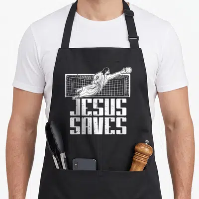 Soccer christian apron - White distressed illustration of Jesus diving for a soccer ball above stacked JESUS SAVES text — shown on a black cotton canvas apron against a white background