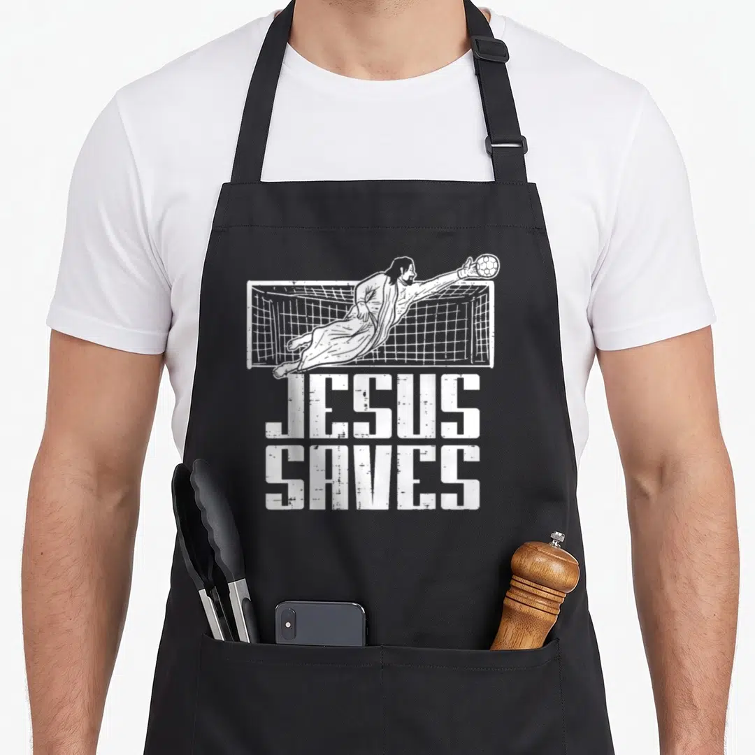 Soccer christian apron - White distressed illustration of Jesus diving for a soccer ball above stacked JESUS SAVES text — shown on a black cotton canvas apron against a white background