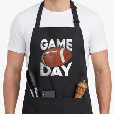 Sport football apron - Brown football between distressed white GAME and DAY text on black background — shown on a black cotton canvas apron against a white background