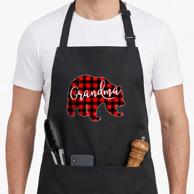 Eve buffalo plaid christmas apron - Red and black plaid bear silhouette with white grandma script text — shown on a black cotton canvas apron against a white background
