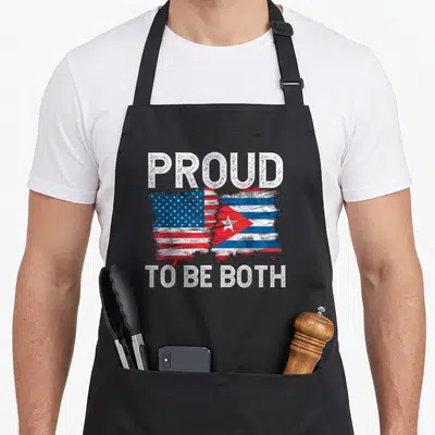 Funny cuban american flag apron - Merged red white blue flags with distressed text proud to be both — shown on a black cotton canvas apron against a white background
