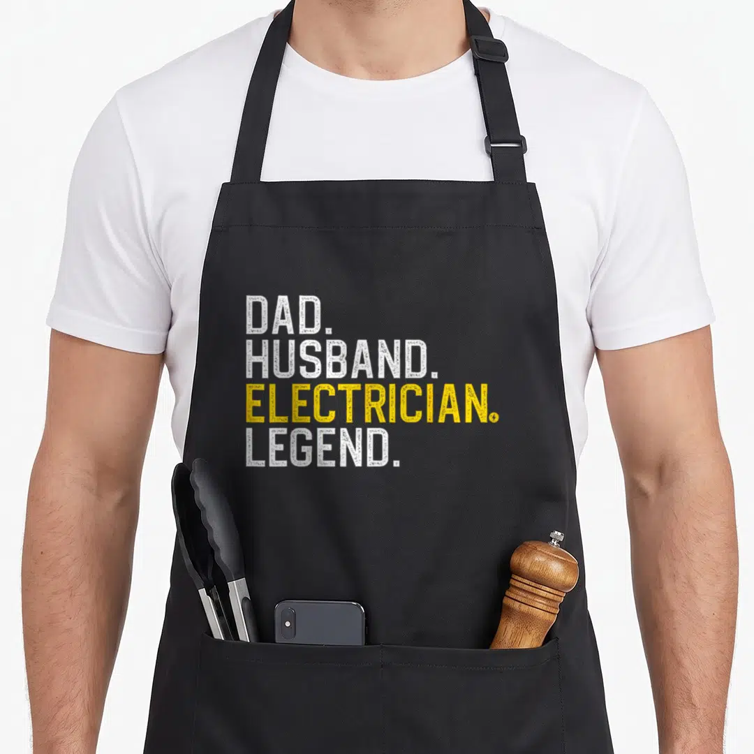 Professional electricians apron - DAD HUSBAND ELECTRICIAN LEGEND stacked text in white and yellow typography — shown on a black cotton canvas apron against a white background