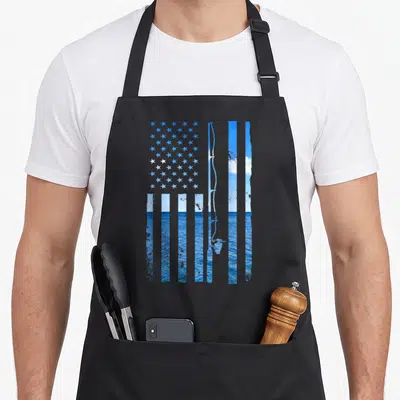 Fish american flag apron - Distressed American flag with blue sky ocean photo and fishing rod silhouette — shown on a black cotton canvas apron against a white background