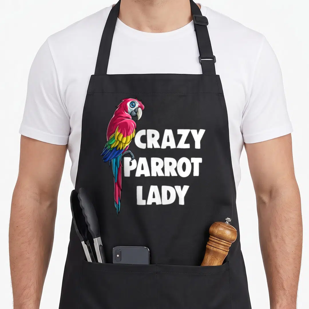 Cute crazy parrot lady apron - Cartoon parrot with pink, yellow, blue feathers beside stacked white text reading CRAZY — shown on a black cotton canvas apron against a white background